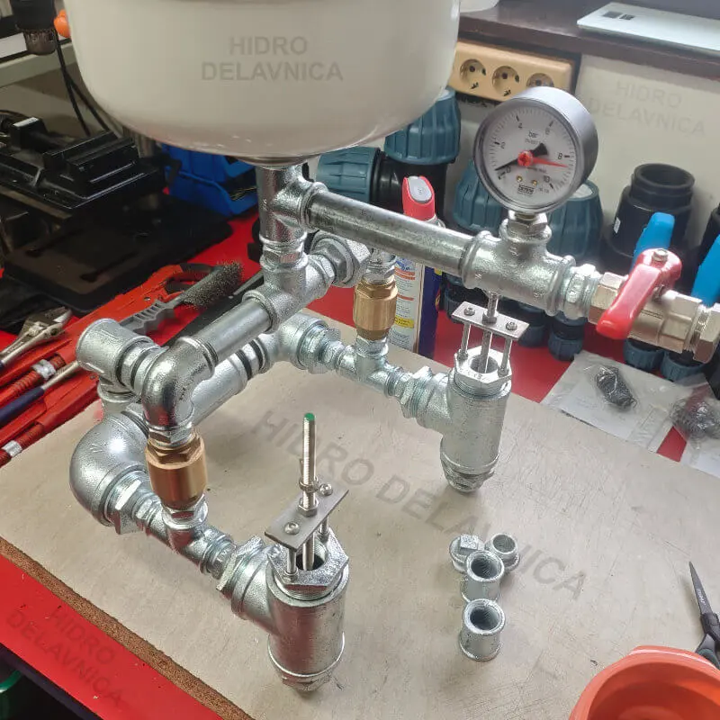 Dvojni hidravlicni vodni oven sestavljen iz vodovodnih fitingov na mizi v delavnici.